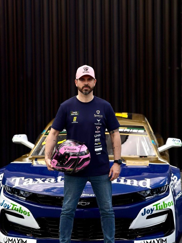 Piloto de NASCAR à frente do carro de corrida, com capacete na mão